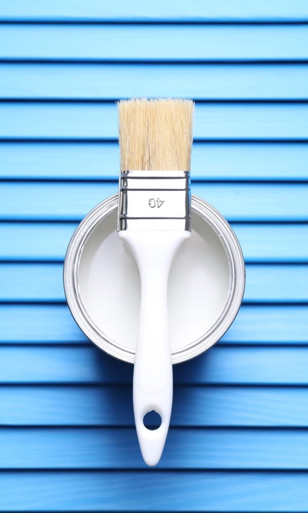 Can of white paint and brush on light blue wooden table, top view