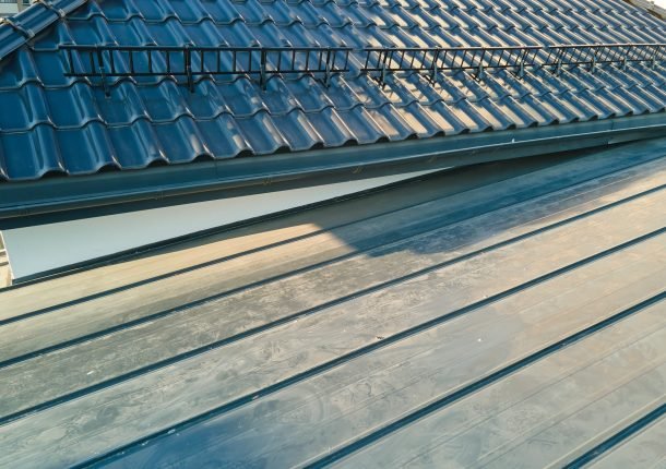 Closeup snow guard for safety in winter on house roof top covered with ceramic shingles. Tiled covering of building.