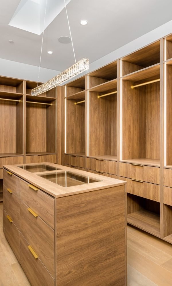 A modern walk-in closet with wooden shelves, drawers, and a central island under bright lighting.