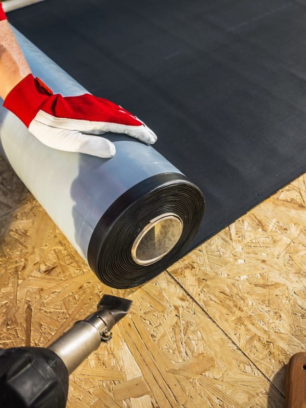 Roof Worker with Roll of EPDM Rubber Membrane Material Preparing to Cover Plywood Roof