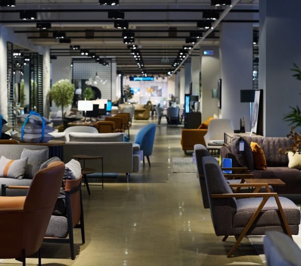 Side view of spacious lobby or coworking area with long aisle dividing two parts of openspace office with armchairs and couches for employees