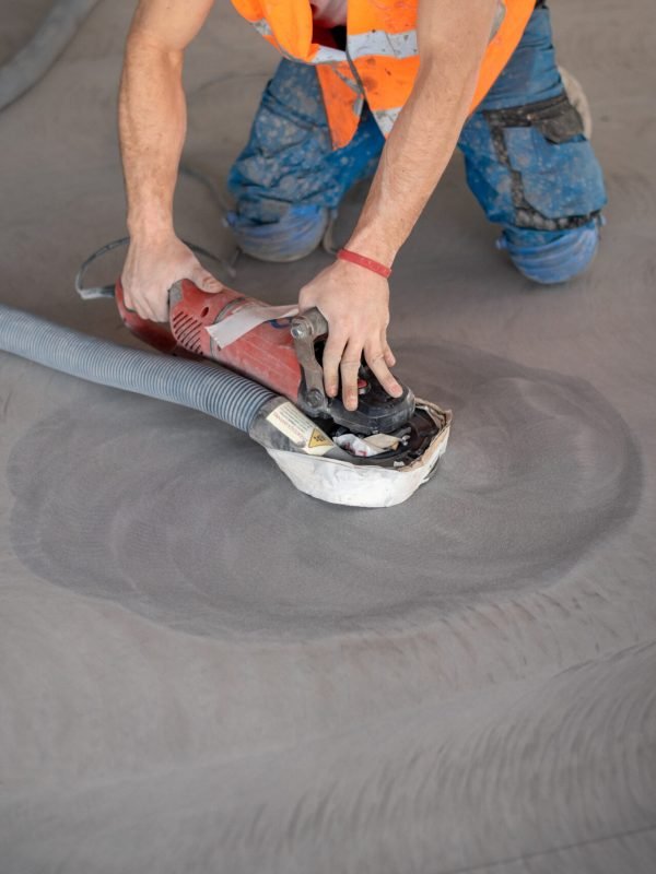 Worker working on the floor of an industrial building. Construction worker producing grout and finishing wet concrete floor.