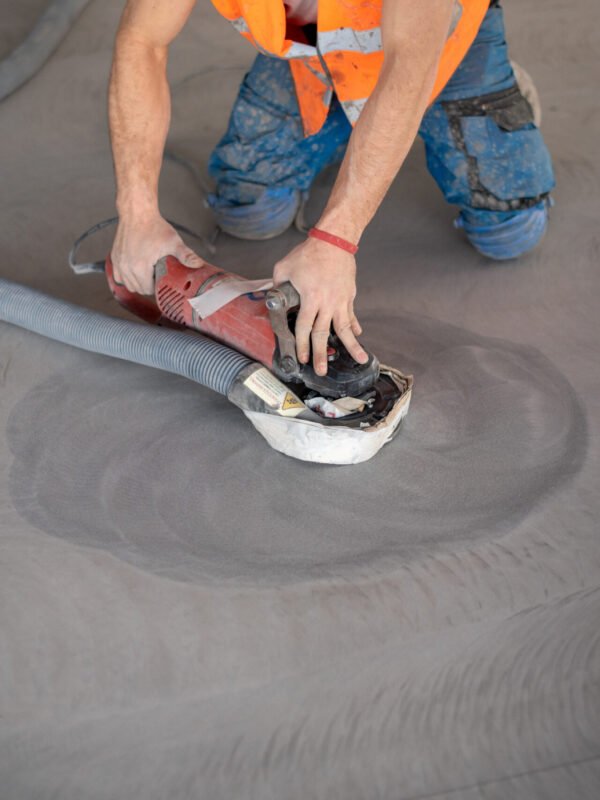 Worker working on the floor of an industrial building. Construction worker producing grout and finishing wet concrete floor.